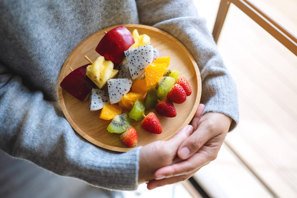 Image rapprochée d'une femme tenant une assiette en bois de fruits frais mélangés sur des brochettes - Photo, image