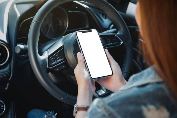 Mockup immagine di una donna in possesso e utilizzando il telefono cellulare con schermo bianco durante la guida di auto - Foto, immagini