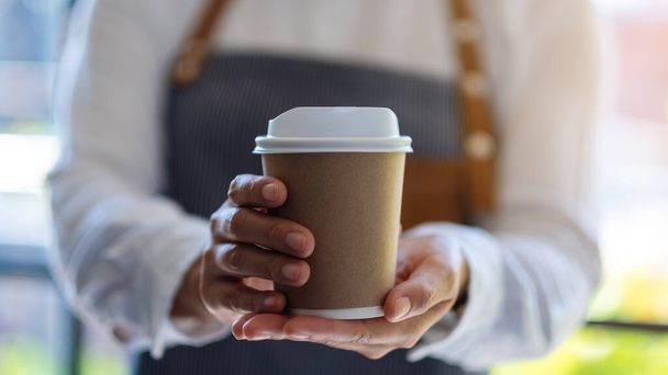 Una cameriera che tiene e serve una tazza di carta di caffè caldo nel caffè - Foto, immagini