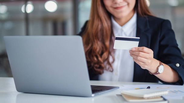 Eine asiatische Geschäftsfrau hält Kreditkarten, während sie Laptop im Büro benutzt - Foto, Bild