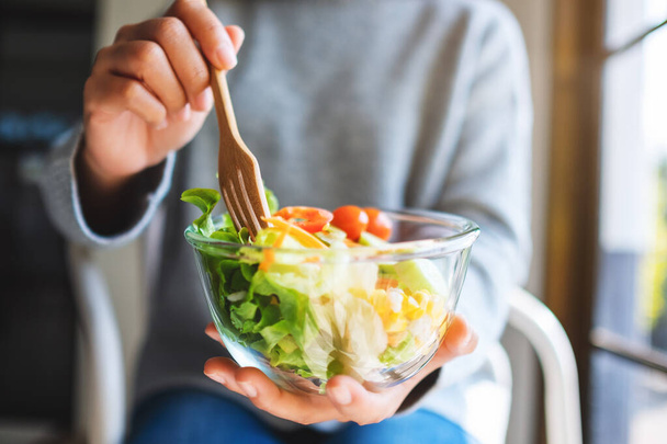 Close-up beeld van een vrouw eten en houden van een kom verse gemengde groenten salade door vork - Foto, afbeelding