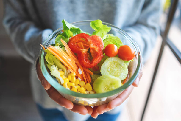 Closeup image of a woman holding a bowl of fresh mixed vegetables salad in hands - Photo, Image