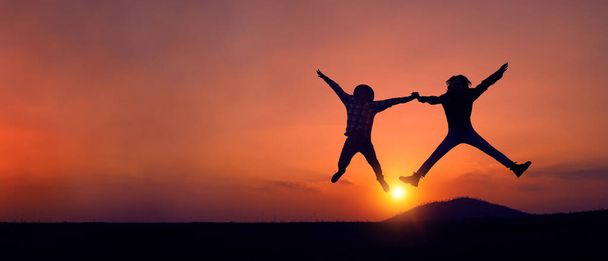 Silhouette of happily couple or friends jumping joyfully on the grass at sunset with copy space. Concept of Inspirational and positive thinking. - Photo, Image