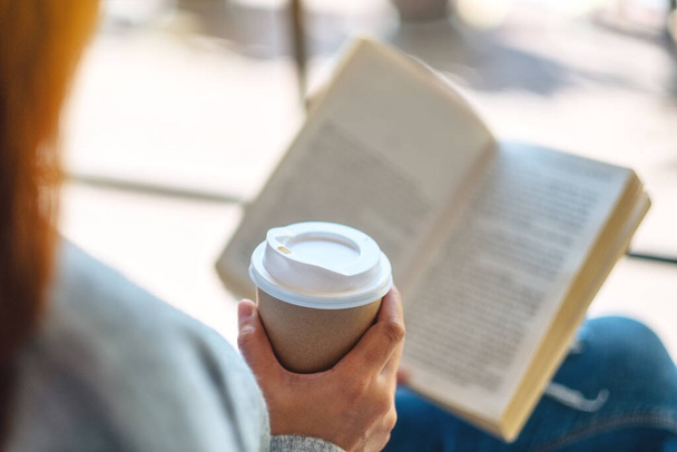 Κοντινή εικόνα μιας γυναίκας που διαβάζει βιβλίο και πίνει καφέ το πρωί - Φωτογραφία, εικόνα
