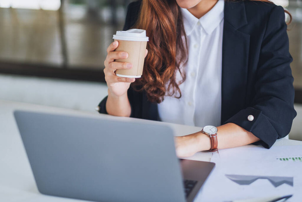 Крупный план деловая женщина, держащая чашку кофе во время работы на ноутбуке в офисе - Фото, изображение