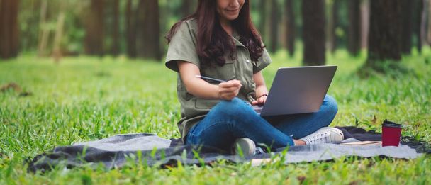 A beautiful asian woman working and typing on laptop keyboard while sitting in the park - Photo, Image