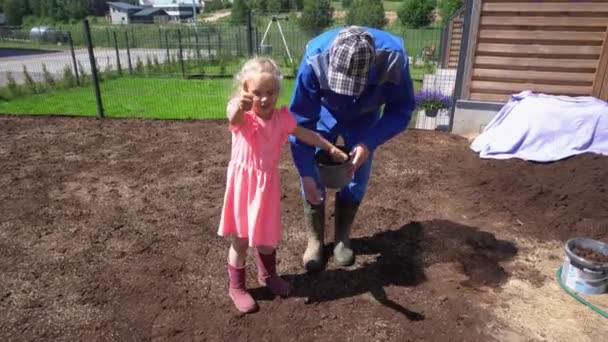 Little daughter girl helping dad with lawn grass seed sowing in apartment yard - Footage, Video