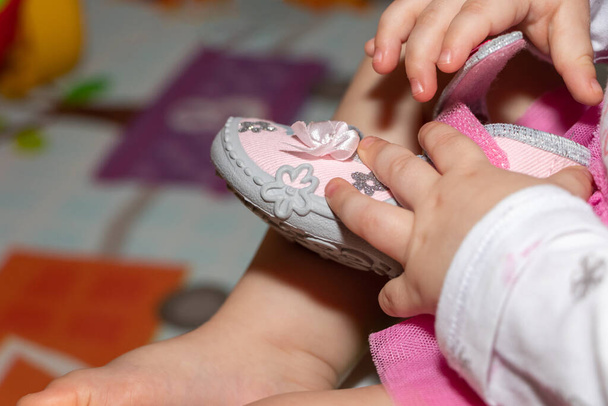 Bir yaşındaki bir kız çocuğu ayakkabılarla oynuyor. Ellerin yakın plan görüntüsü. - Fotoğraf, Görsel