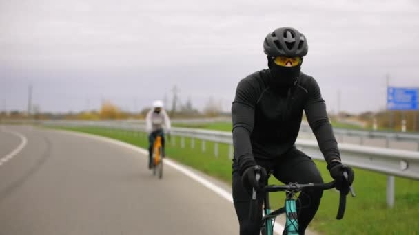 Két sportoló biciklin edz. Autóval mennek az autópályán. Edzés a hideg évszakban. 4K - Felvétel, videó