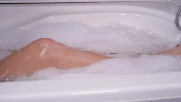 Gros plan des jambes féminines nues dans un bain avec beaucoup de mousse, elle les déplace lentement. - Séquence, vidéo