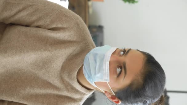 Lähikuva nuori intialainen nainen naamio näyttää pois, kommunikoi lääkärin kotona kirkkaassa huoneessa pandemian aikana, pystysuora video - Materiaali, video