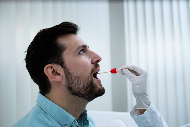 Detailní záběr mladého muže provádějícího PCR test v ordinaci lékaře během epidemie koronového viru. - Fotografie, Obrázek