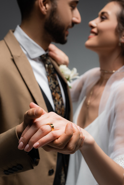 Bride with wedding ring on finger holding hand of arabian groom on blurred background isolated on grey  - Photo, Image