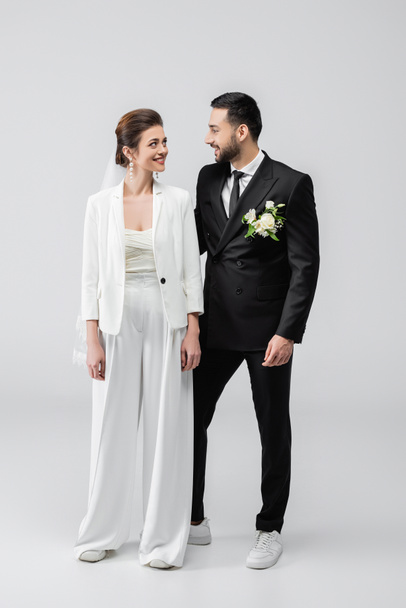 Sposa sorridente guardando lo sposo arabo in abito su sfondo bianco  - Foto, immagini