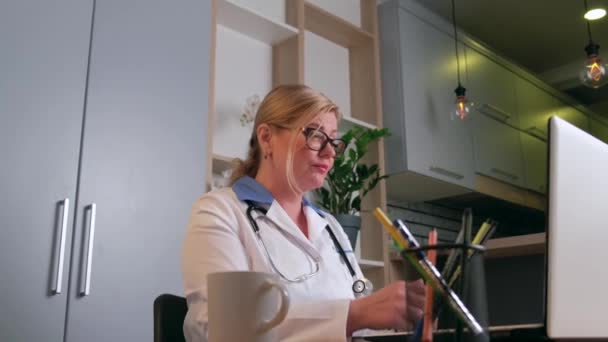 Sivukuva video blondi nainen yllään lääketieteellinen takki puhuu potilaan kanssa verkossa kannettavan - Materiaali, video