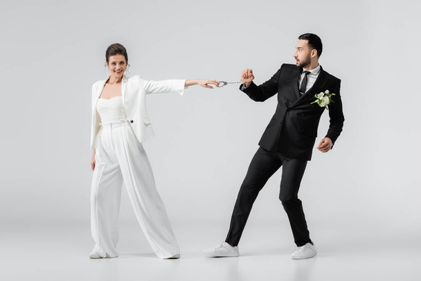 Positive Braut zieht Handschellen muslimischer Bräutigam auf weißem Hintergrund - Foto, Bild