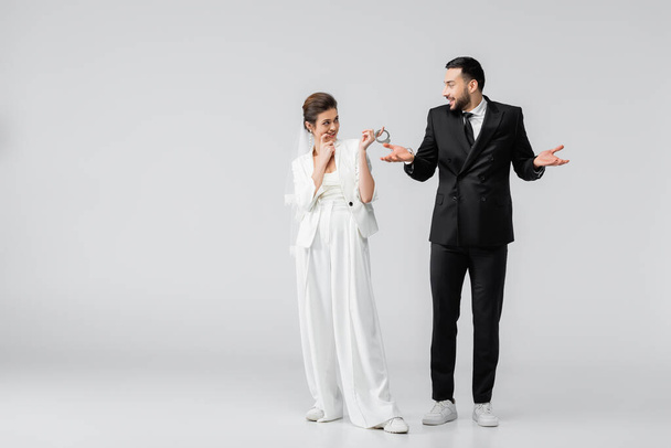 笑顔女性でベールと結婚式スーツ保持手錠近くアラビア語新郎ショー混乱ジェスチャー上の白の背景 - 写真・画像