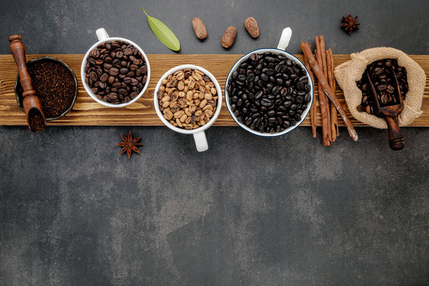 Brown unroasted and dark roasted coffee beans in coffee cup with scoops setup on dark stone background. - Photo, Image
