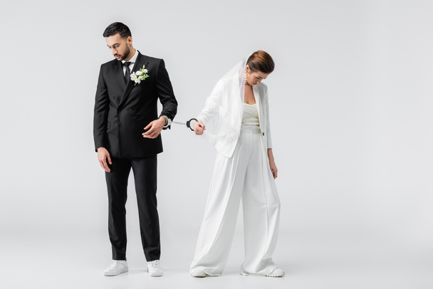 Trauriger Bräutigam und Braut in Handschellen auf weißem Hintergrund - Foto, Bild