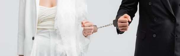 Обрізаний вид нареченого і нареченого в наручниках ізольований на сірому, банер
  - Фото, зображення