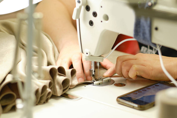 Las manos femeninas cosiendo tela blanca en la máquina de fabricación profesional en el lugar de trabajo. Vista de cerca del proceso de costura. Fondo claro y borroso - Foto, Imagen