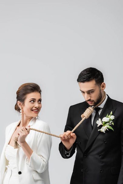Mosolygó menyasszony kezében kötél csúszós csomó nyakán muszlim vőlegény elszigetelt szürke  - Fotó, kép