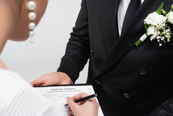 Vista ritagliata di sposa firma contratto di matrimonio vicino sposo isolato su grigio  - Foto, immagini