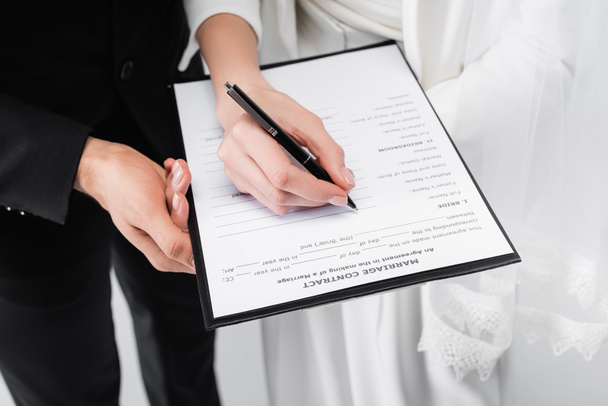 Vista recortada de pareja firmando contrato de matrimonio aislado en gris  - Foto, imagen