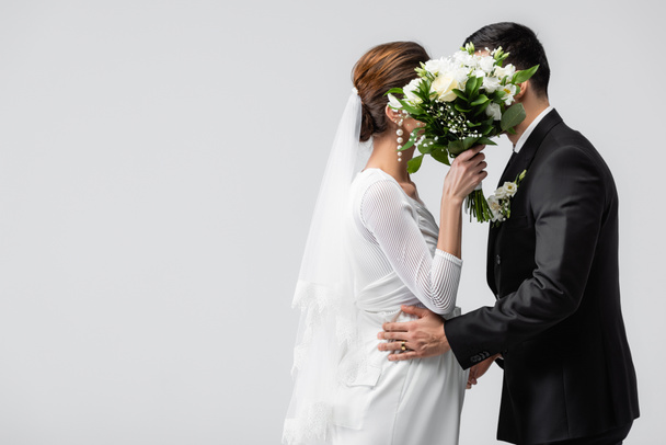 妊娠中の花嫁と新郎は灰色で隔離された花束の後ろに隠れて  - 写真・画像