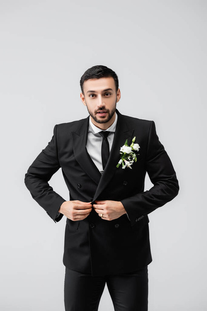 Young arabian groom buttoning jacket isolated on grey  - Photo, Image