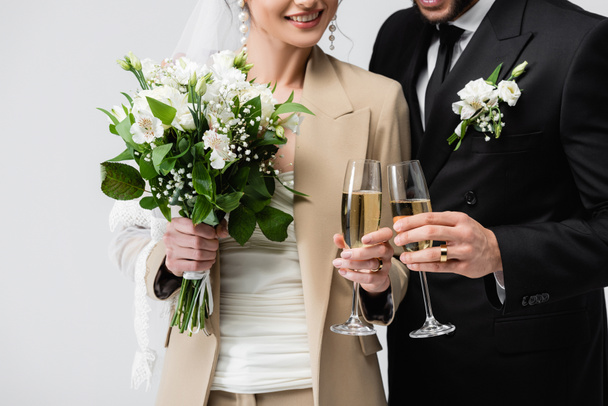 Vue recadrée de jeunes mariés souriants toastant au champagne isolé sur gris  - Photo, image