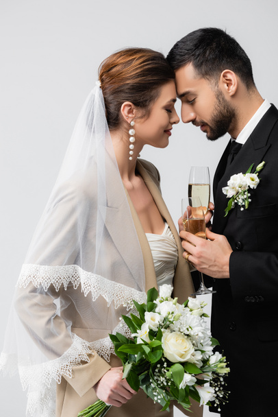 elegant bride and young arabian fiance standing face to face with closed eyes isolated on grey - Photo, Image