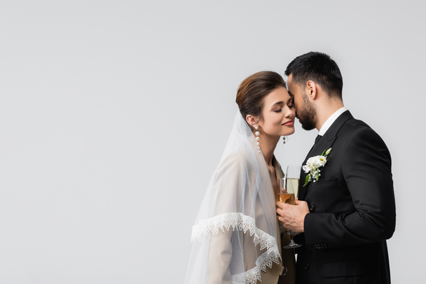 elegant, happy interracial newlyweds holding champagne glasses isolated on grey - Photo, Image