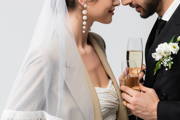 частичный вид элегантной невесты и мусульманского мужчины, стоящего лицом к лицу с бокалами шампанского, изолированными на сером - Фото, изображение