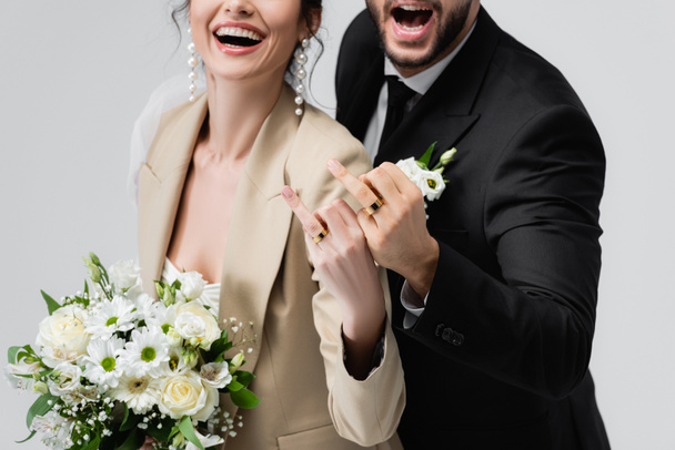 Yeni evli çiftin gri renkte izole edilmiş evlilik yüzüklerini gösteren kısmi görüntüsü - Fotoğraf, Görsel