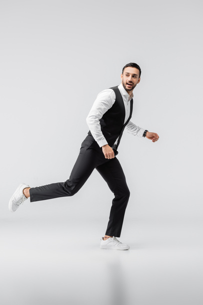 Модный мужчина в полный рост смотрит в сторону во время бега на сером - Фото, изображение