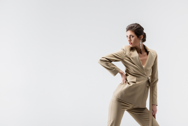 fashionable woman in beige pantsuit posing with hand on hip isolated on grey - Photo, Image