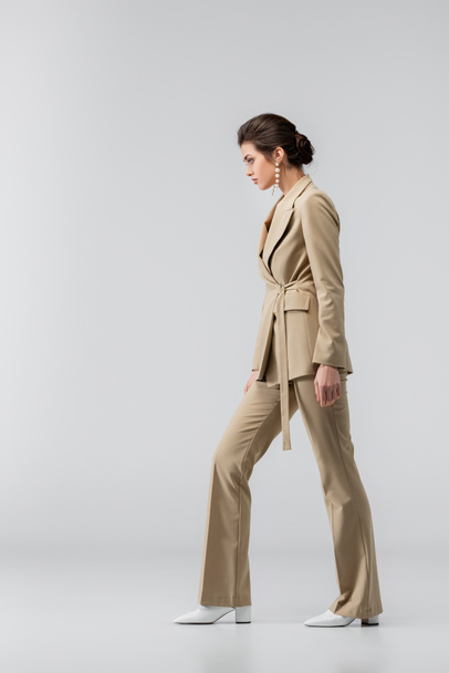 longitud completa de la mujer en traje de pantalón elegante de pie en gris, vista lateral - Foto, imagen
