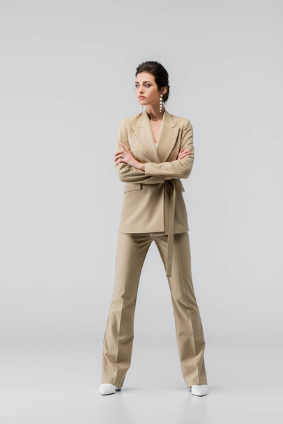 full length view of stylish woman looking away while posing with crossed arms on grey - Photo, Image