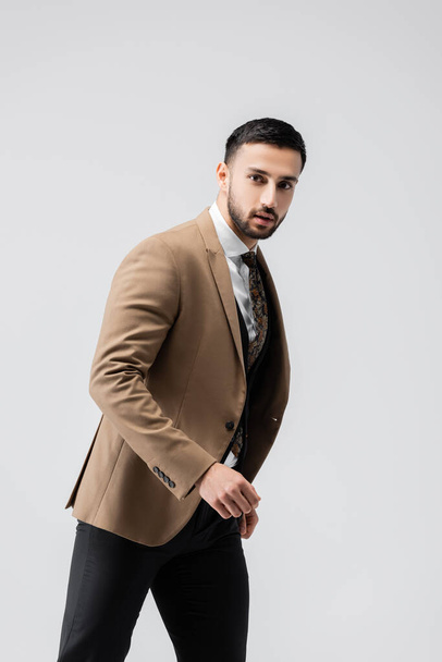 uomo arabo alla moda guardando la fotocamera mentre camminava isolato sul grigio - Foto, immagini
