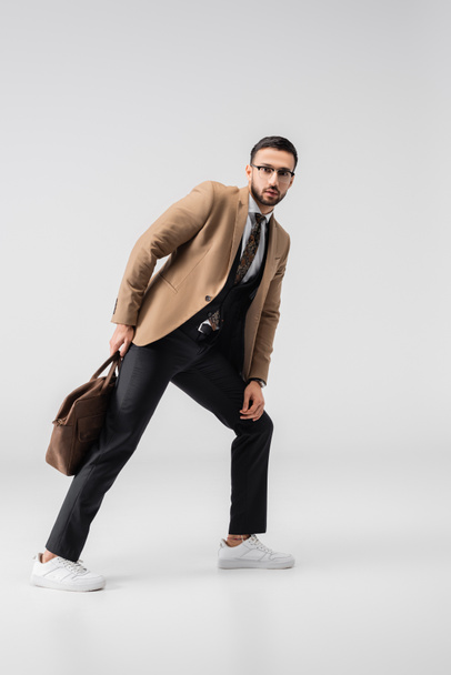 teljes hosszúságú kilátás trendi muszlim férfi néz kamera, miközben pózol bőr táska szürke - Fotó, kép