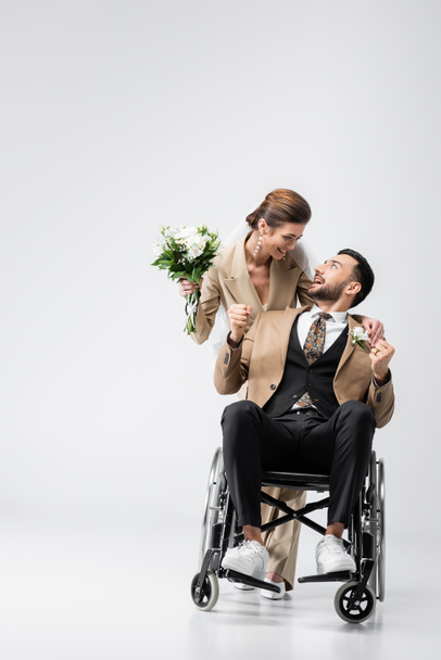 інвалідний мусульманський наречений, що показує жест виграшу біля щасливої нареченої з весільним букетом на сірому
 - Фото, зображення