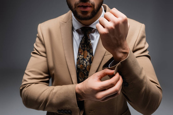 abgeschnittene Ansicht von stilvollen muslimischen Mann Knopfleiste Ärmel auf Blazer auf grau - Foto, Bild