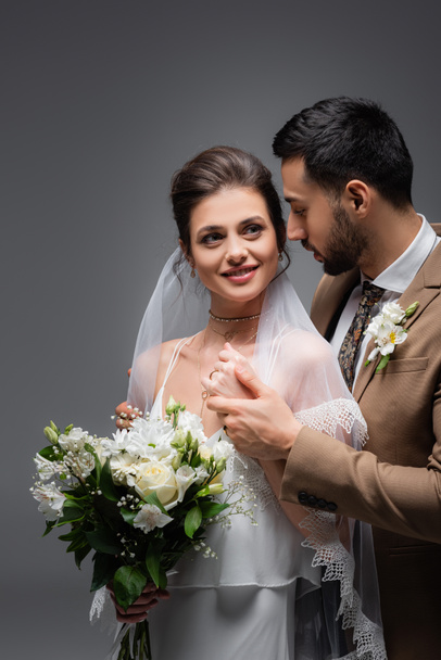 happy woman with wedding bouquet near muslim fiance isolated on grey - Photo, Image