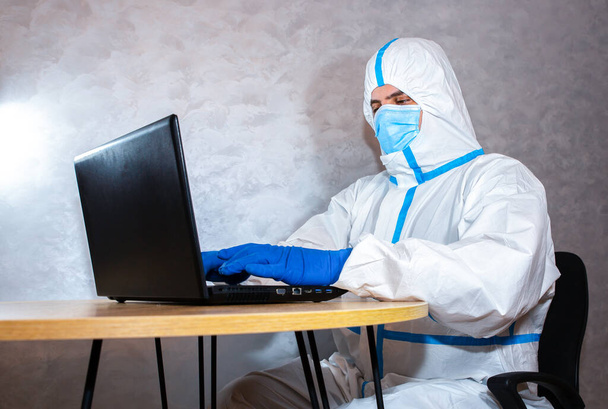 Doctor wearing medical protective suit, medical mask and gloves working on laptop. Protection mers by virus epidemic. Coronavirus (COVID-19). Healthcare concept. Remote work in a pandemic covid. - Photo, Image