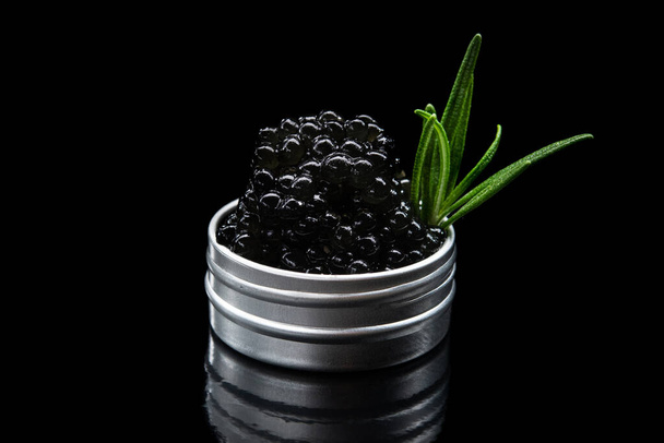Black caviar in a metal container with green fresh rosemary isolated on a background - Photo, Image