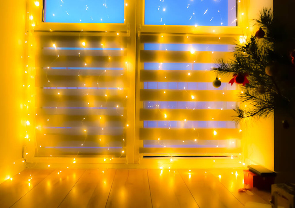 Gyönyörű homályos villogó sárga fény. Otthoni dekoráció koszorúval az ablakon, éjszakai Bokeh világítás. Ünnepi háttér. - Fotó, kép