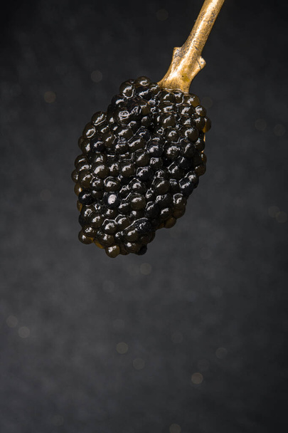 Close-up van gouden vintage lepel gevuld met zwarte kaviaar op donkere achtergrond. rijk, gastronomisch, duur eten. - Foto, afbeelding