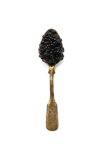 Vintage old spoon completely filled with black caviar isolated on a white background. top view - Photo, Image