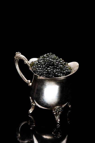 Black sturgeon caviar in retro vintage dish isolated on a black background. seafood diet food - Photo, Image